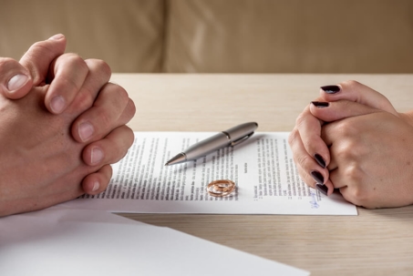 A table with divorce papers and a ring with two set of hands resting on opposite sides of the table